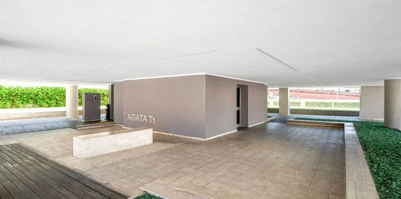 A covered outdoor courtyard with paved flooring, a low planter, and green landscaping.