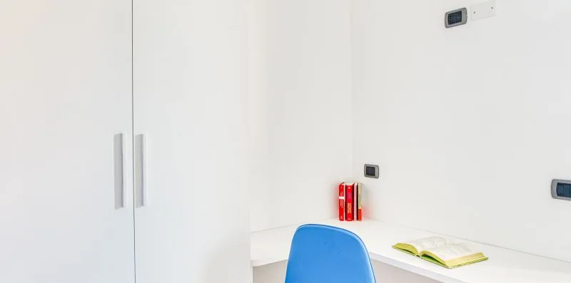 A bright study area with a desk, blue seating, and wall cabinets.