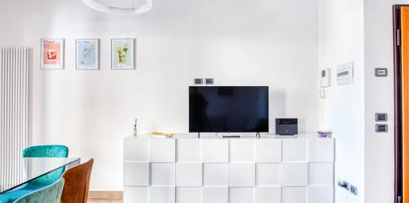 A bright living area with a television on a white media console and framed prints.