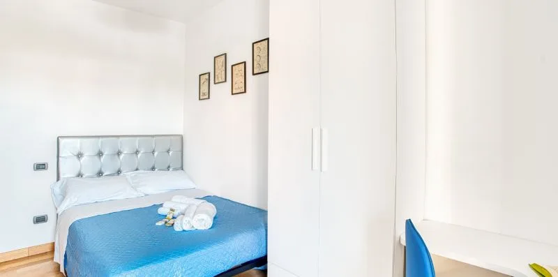 A bedroom with a bed covered by blue bedding and a white wardrobe.