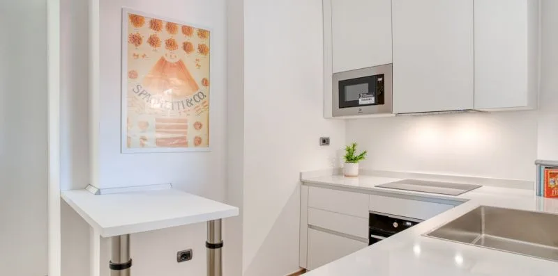 A bright white kitchen with built-in appliances and a small dining counter.