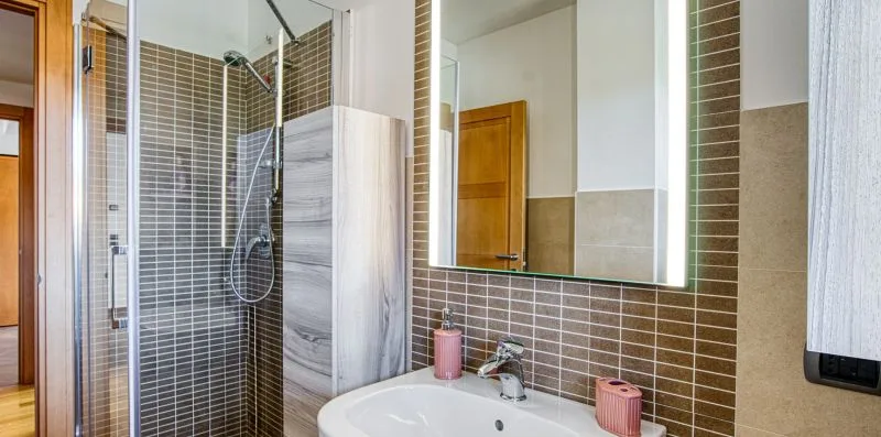 A bathroom with a glass shower, tiled walls, and a sink beneath a large mirror.