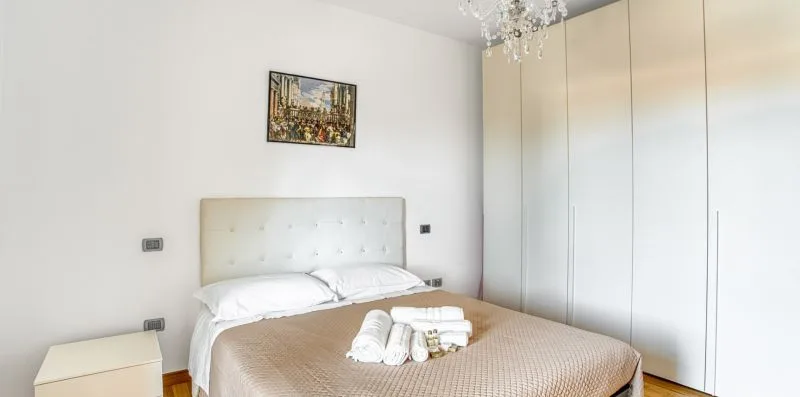 A bright bedroom with a bed, white bedding, and built-in wardrobes.