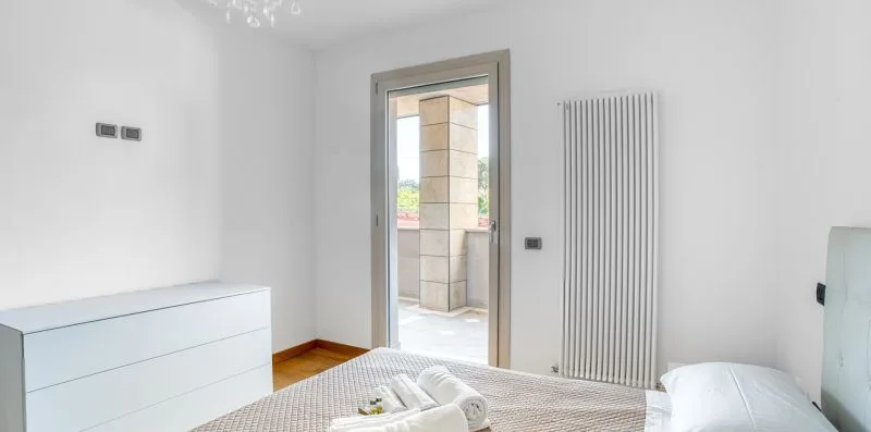A bright bedroom with a bed, white dresser, and tall radiator.