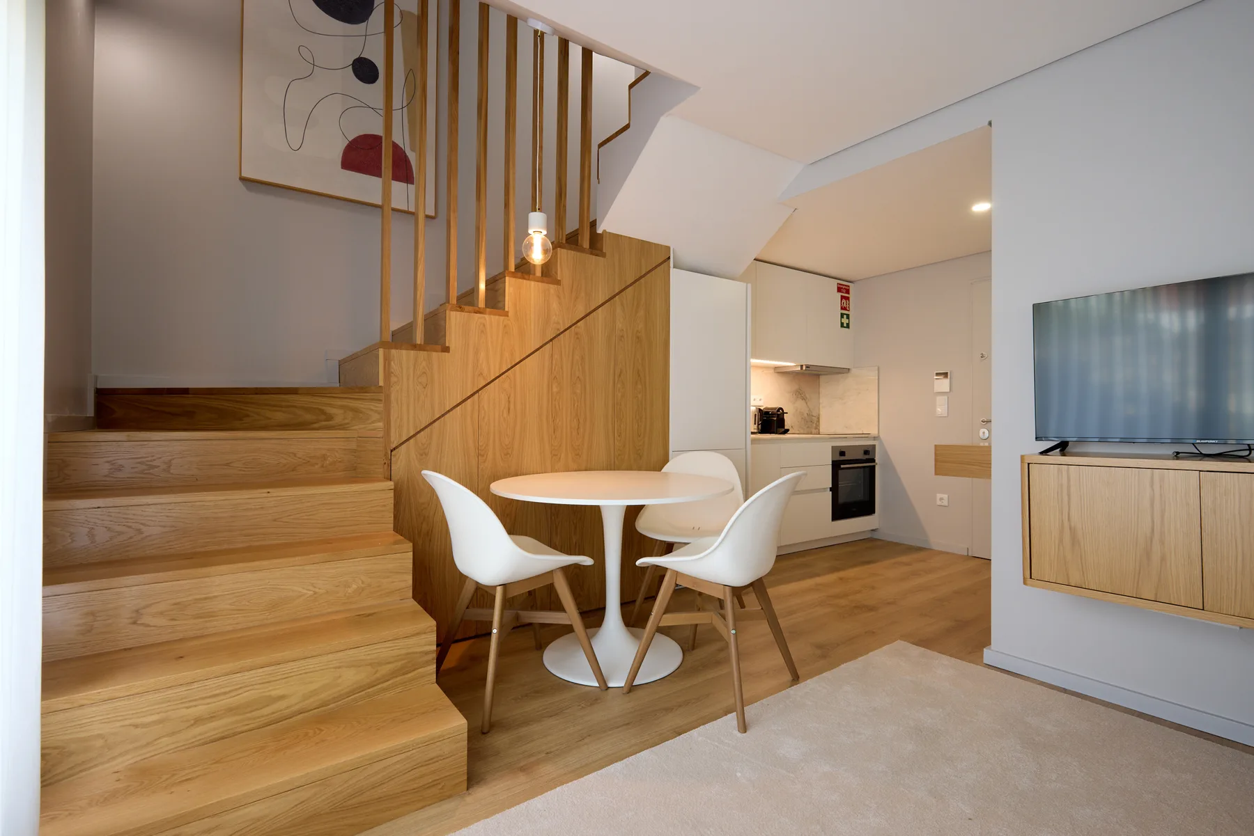 A compact living area with wooden stairs, a small dining table, and a kitchenette.
