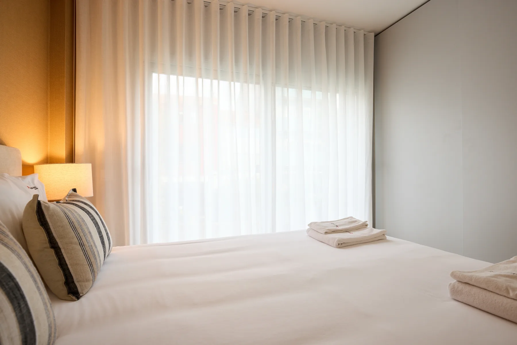 Un dormitorio con ropa de cama blanca y una gran ventana con cortinas.