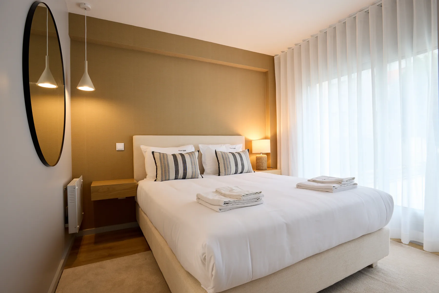 Un dormitorio con una cama bien tendida y cortinas de suelo a techo.