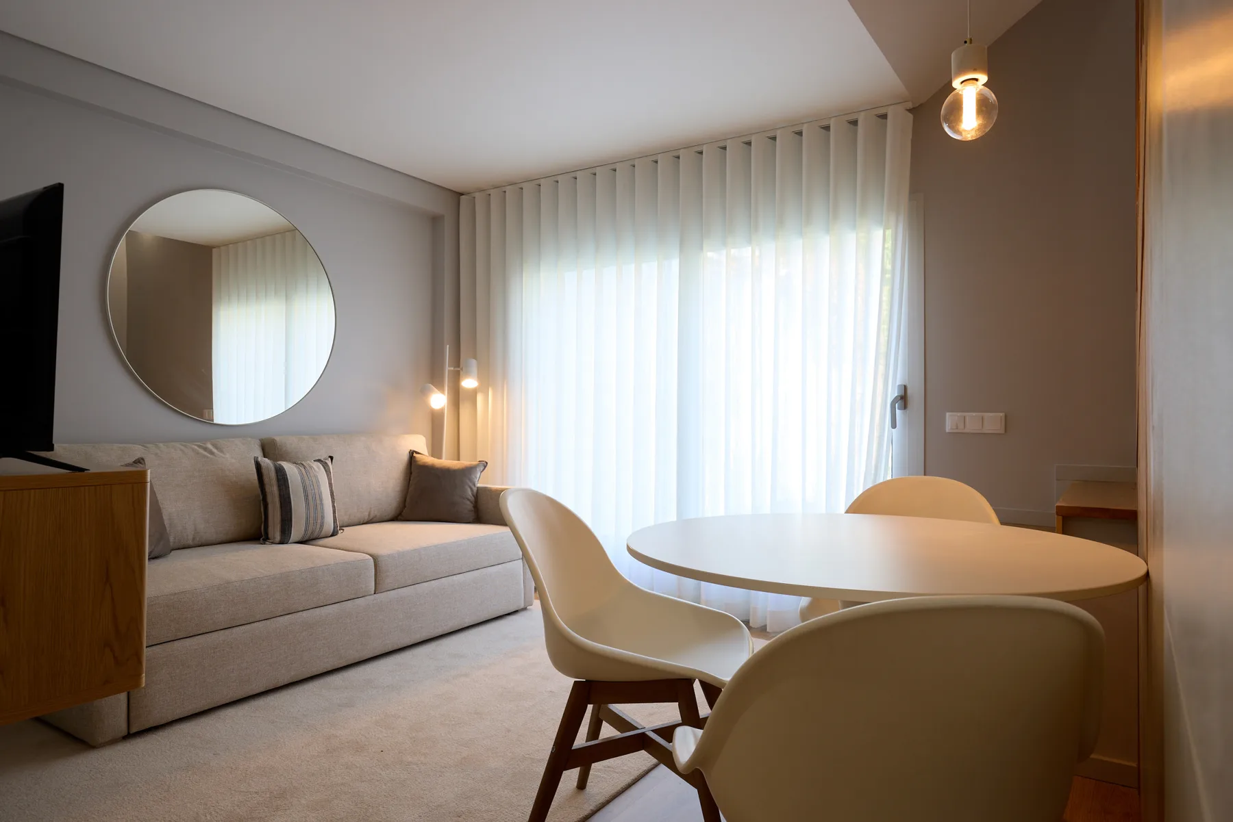 Zona de sala y comedor con asientos junto a una gran ventana con cortinas.