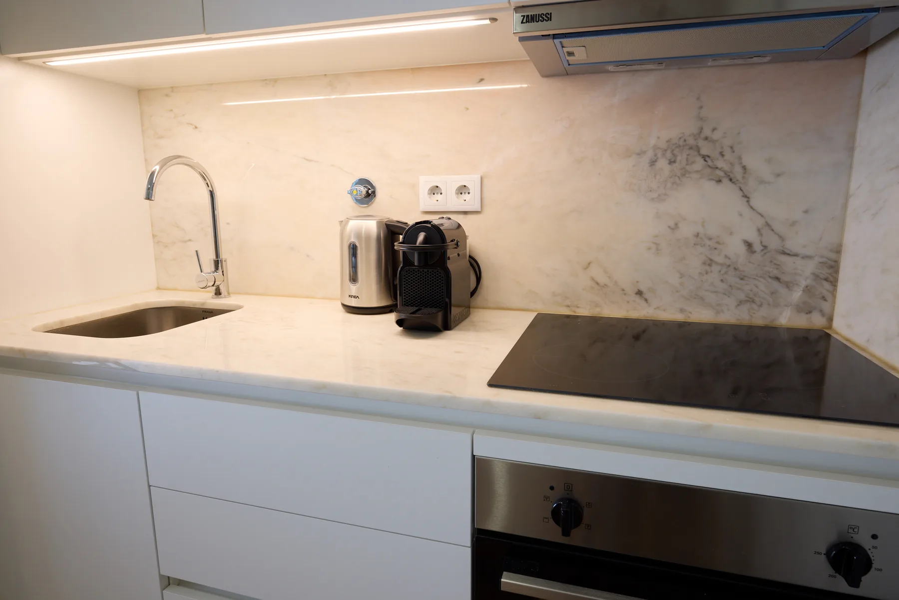 Una encimera de cocina moderna con fregadero, cafetera y placa de cocción.