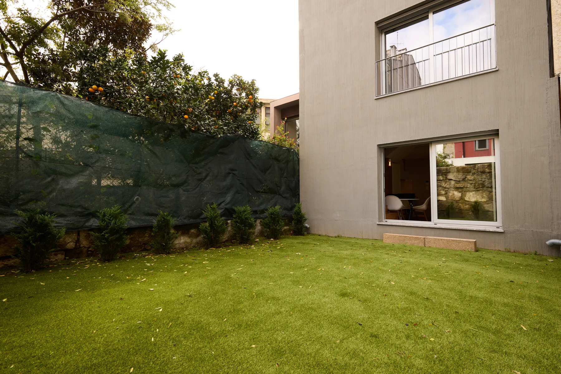 A grassy garden beside a modern building, with large windows and leafy trees.