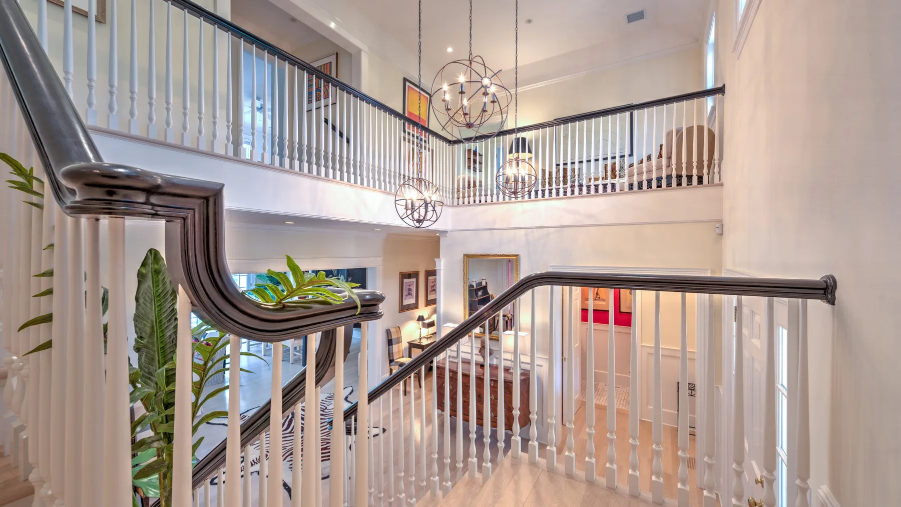 Una luminosa escalera interior de dos niveles con barandillas blancas y luces colgantes.