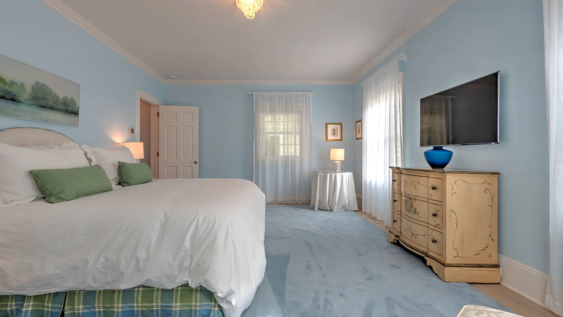 Un dormitorio con una cama, paredes celestes y una cómoda de madera.