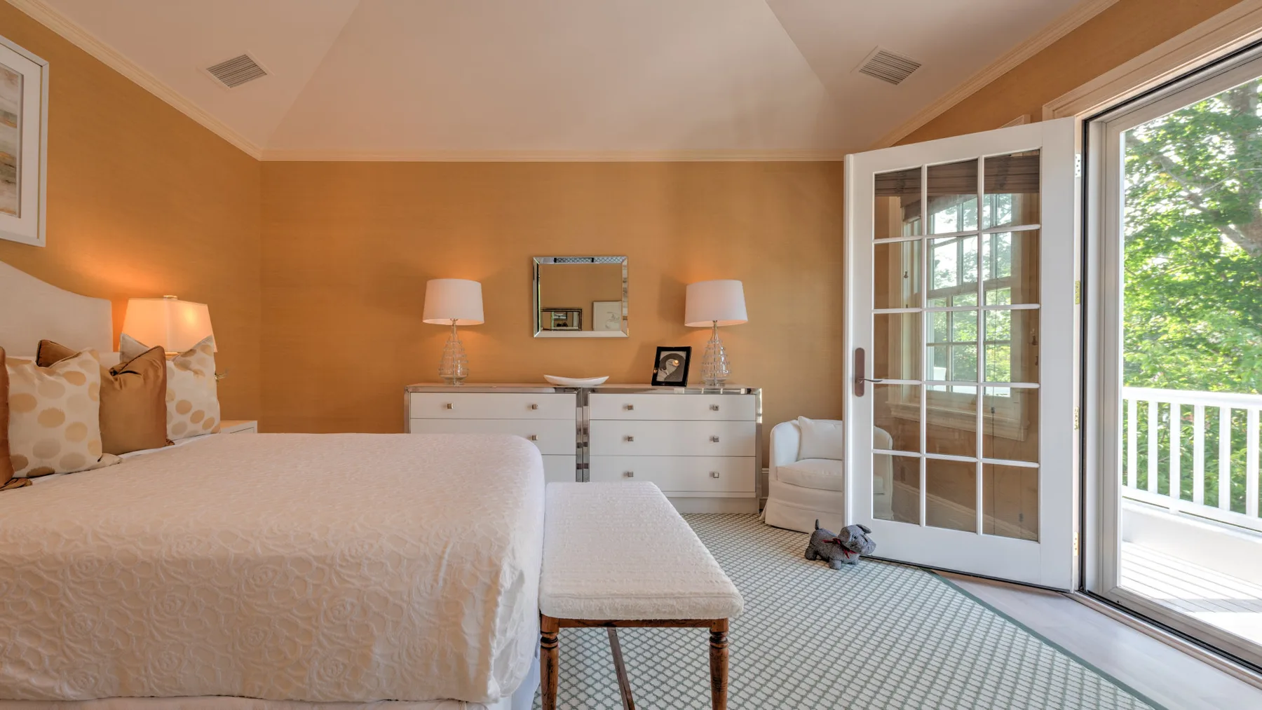 Un dormitorio luminoso con una cama, una cómoda y puertas de vidrio que dan a un patio.