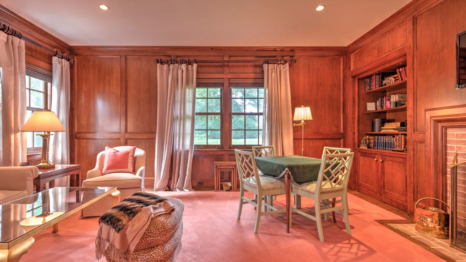 Una sala revestida de madera con mesa de comedor, asientos y ventanas con cortinas.