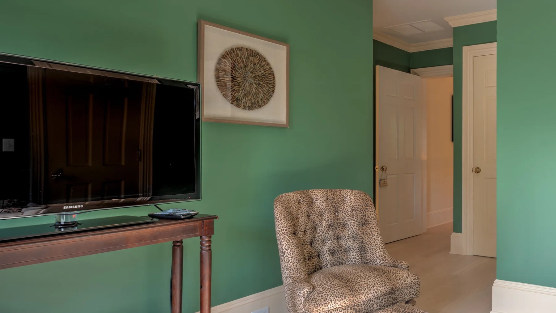 Una habitación de paredes verdes con un televisor, una mesa pequeña y un sillón tapizado.