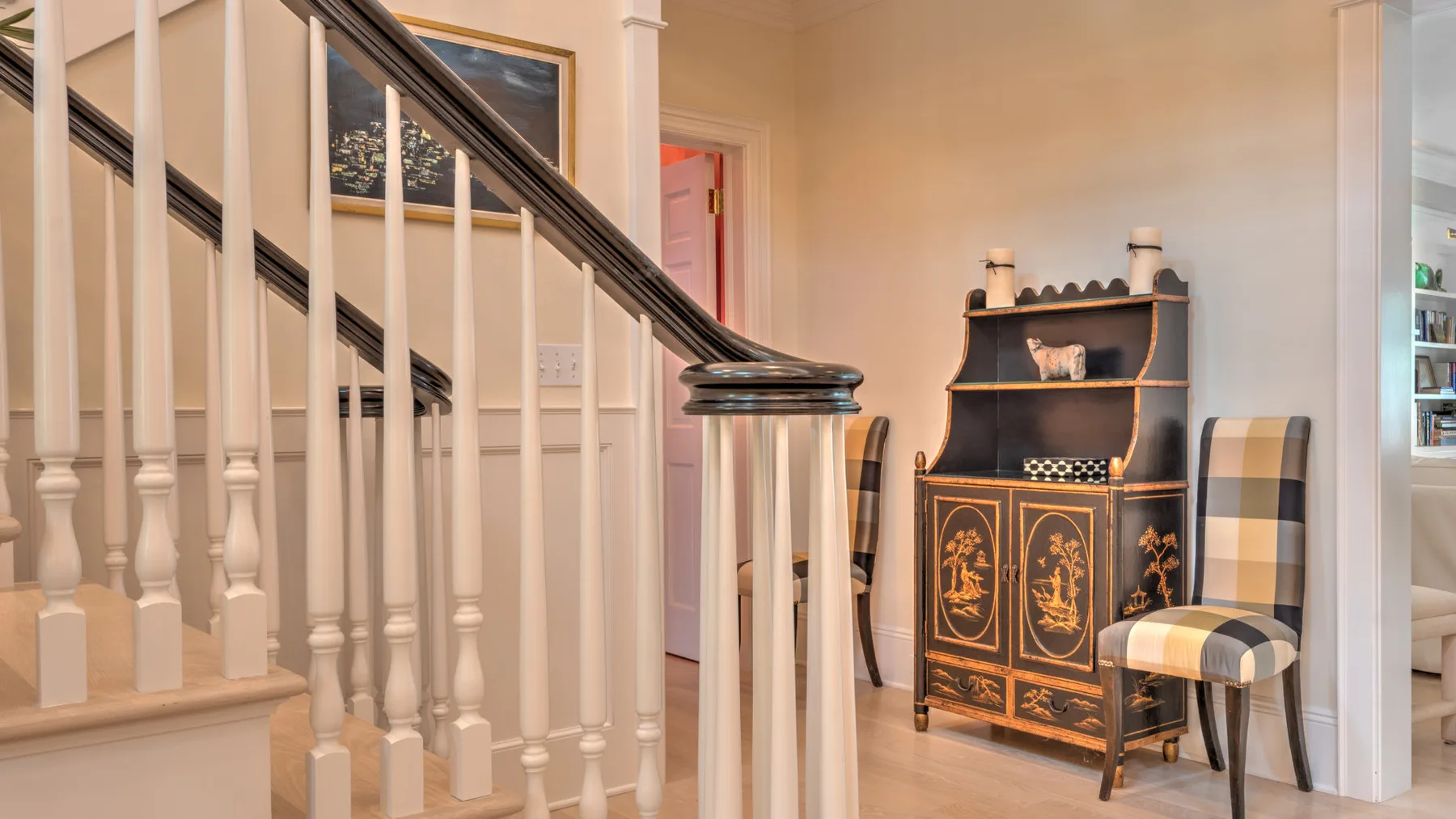 Una escalera junto a un armario oscuro y dos sillas estampadas en una habitación de tonos cálidos.