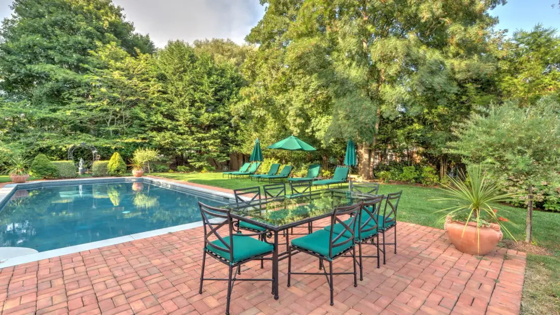 Una zona de comedor al aire libre junto a una piscina, rodeada de árboles y vegetación.