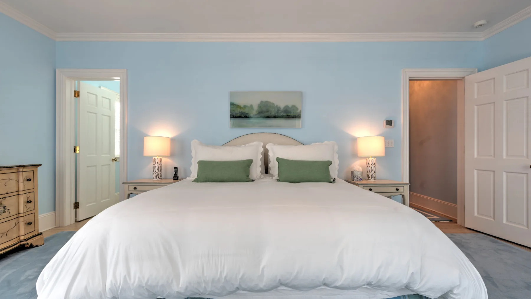 Un dormitorio con una cama grande, almohadas verdes y lámparas a ambos lados.