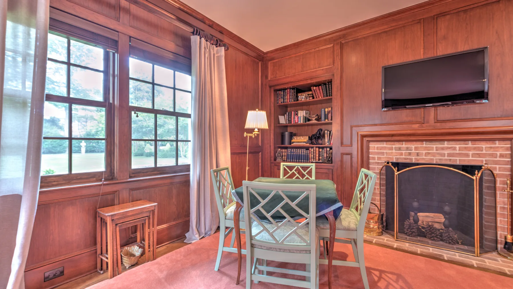 Una sala revestida de madera con una mesa junto a una chimenea y grandes ventanas.