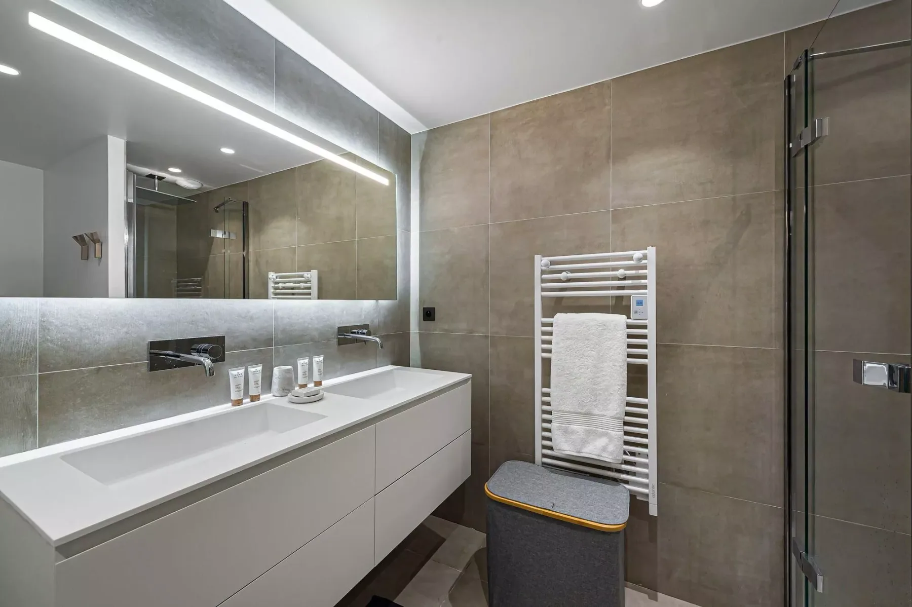 Un baño moderno con un lavabo largo, espejo de pared y radiador toallero.