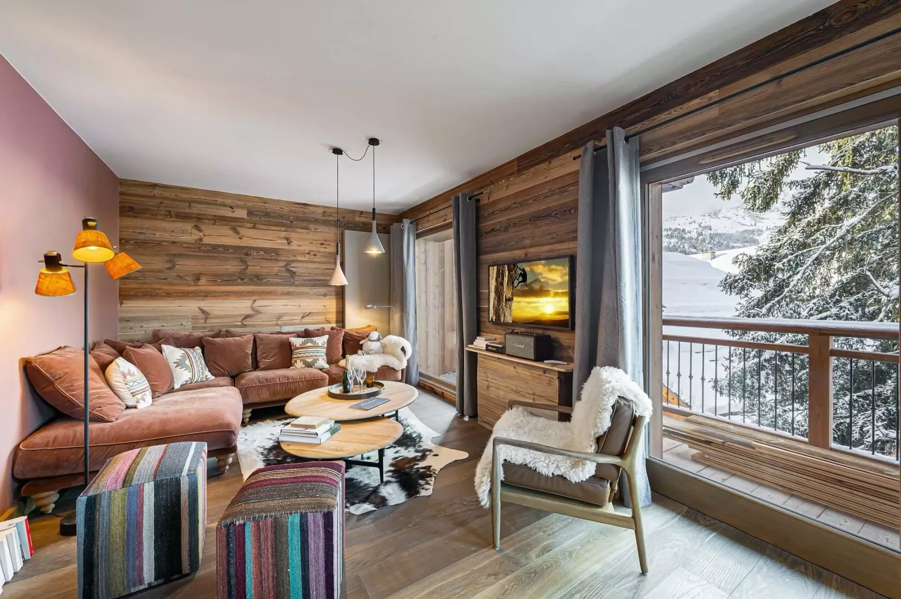 Una sala de estar con asientos, un televisor y grandes ventanales con vistas a un paisaje nevado.