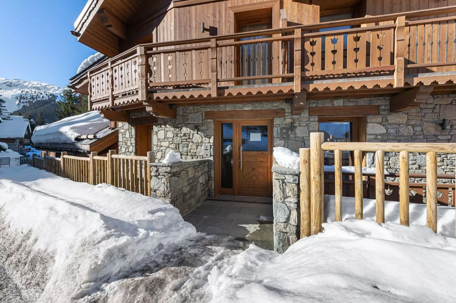 Entrada de un chalet de madera con paredes de piedra y suelo cubierto de nieve.