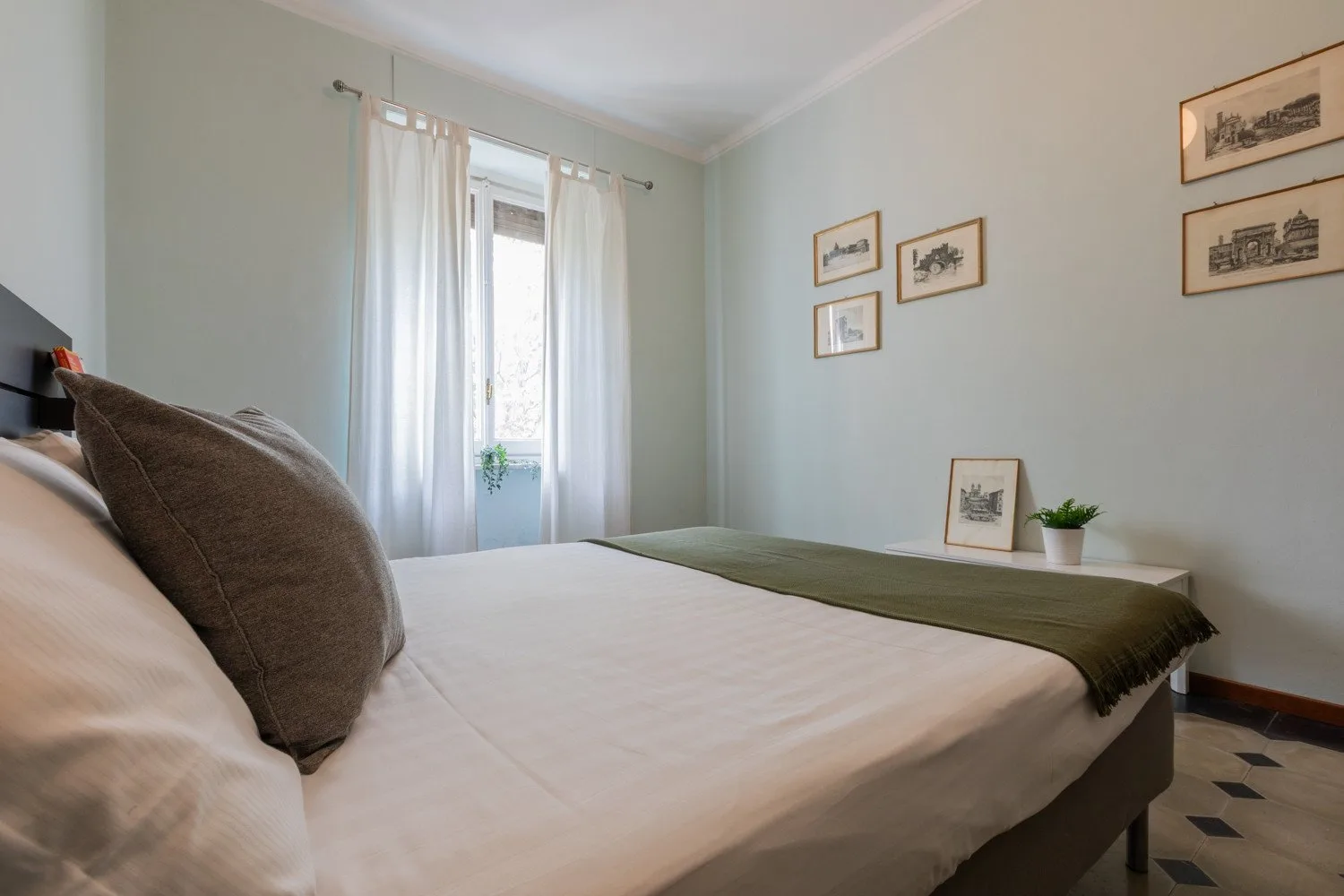 Un dormitorio con una cama, una manta verde y una ventana luminosa con cortinas.