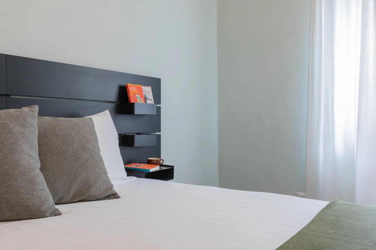Un dormitorio con una cama bien tendida y un cabecero oscuro con estantes.