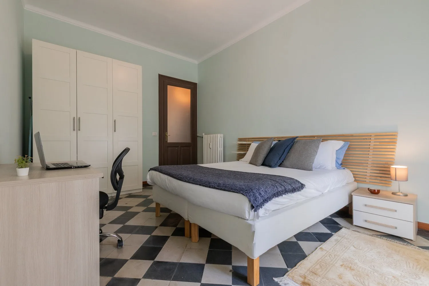 Un dormitorio con una cama grande, un armario y suelo de baldosas blancas y negras.