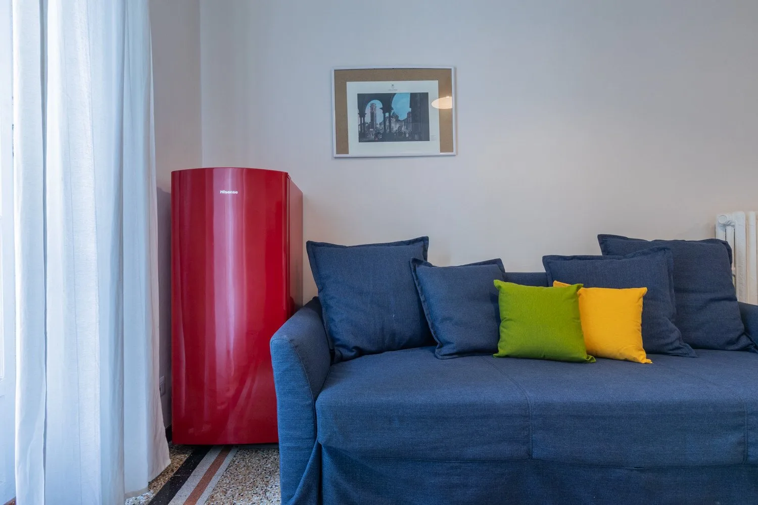 Una sala de estar con asientos azules y un mueble rojo junto a la ventana.