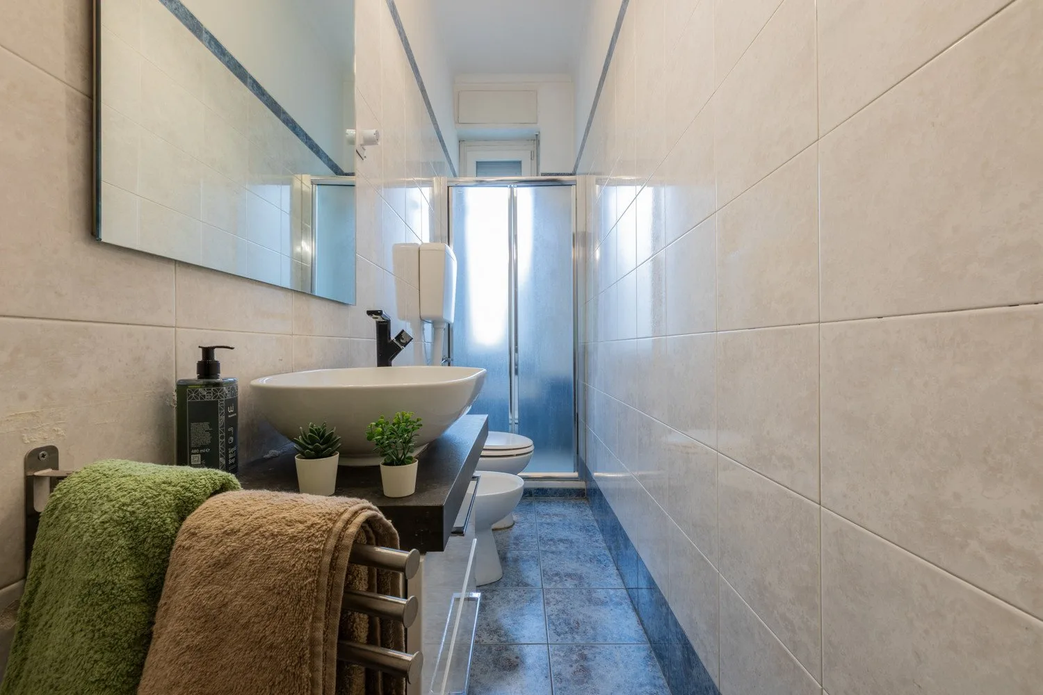 Un baño estrecho con azulejos, lavabo, espejo y ducha al fondo.