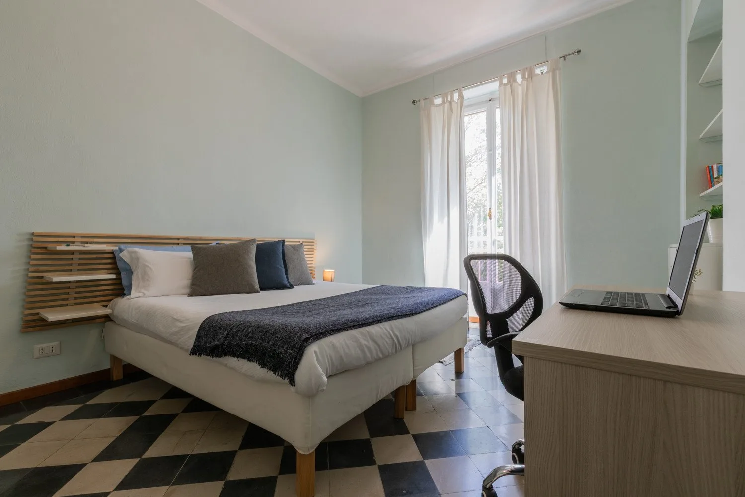 Un dormitorio con una cama y un escritorio junto a una ventana luminosa.