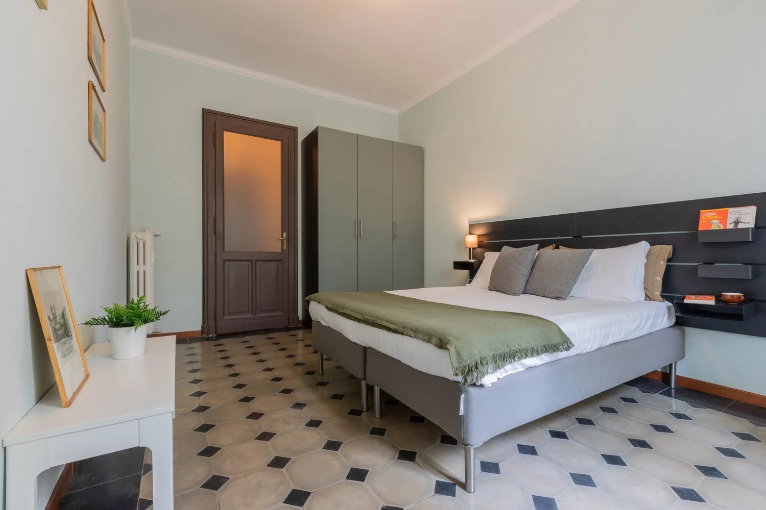 Un dormitorio con una cama grande, cabecero gris y paredes verde claro.