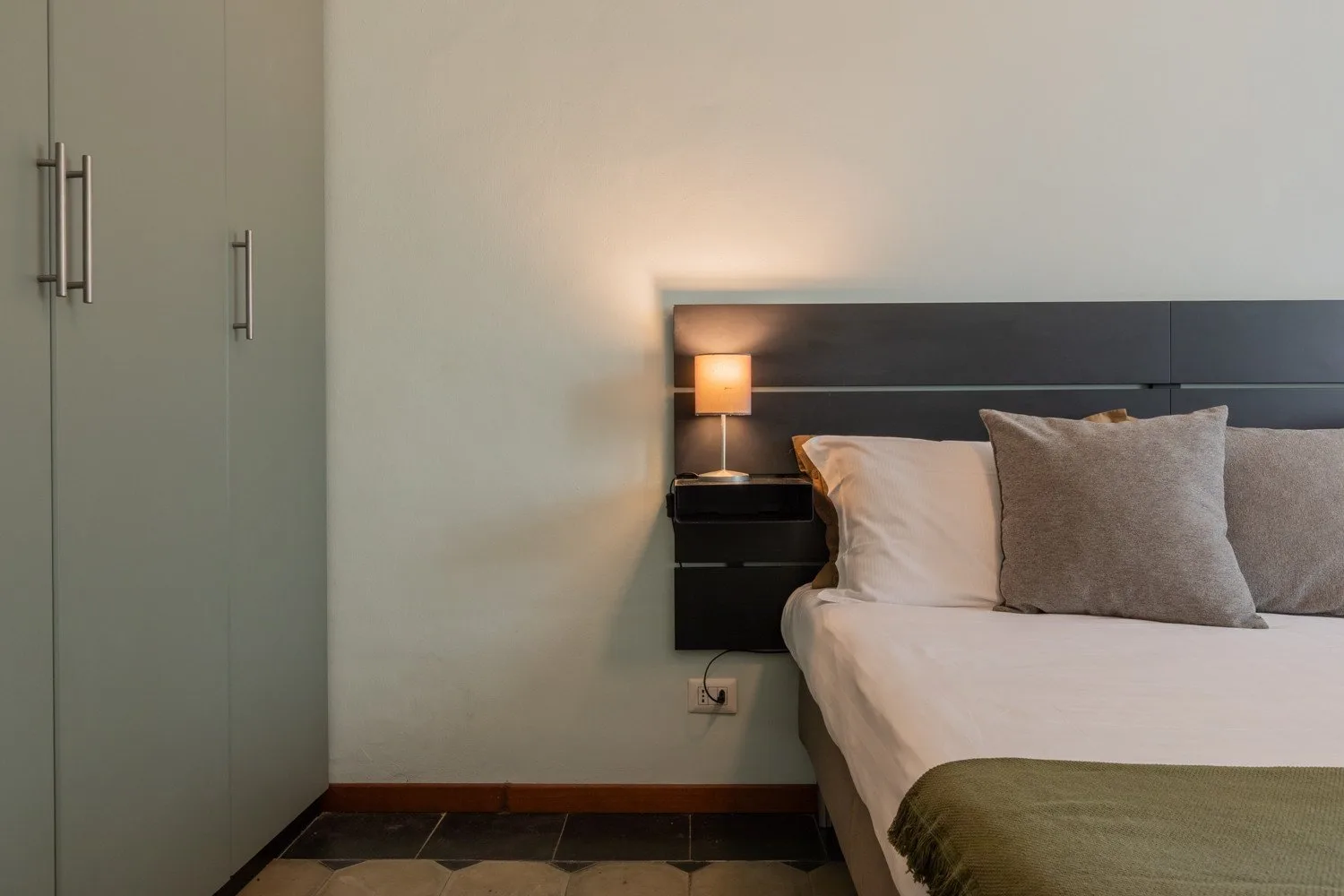 Un dormitorio con una cama, almohadas y una lámpara de noche.