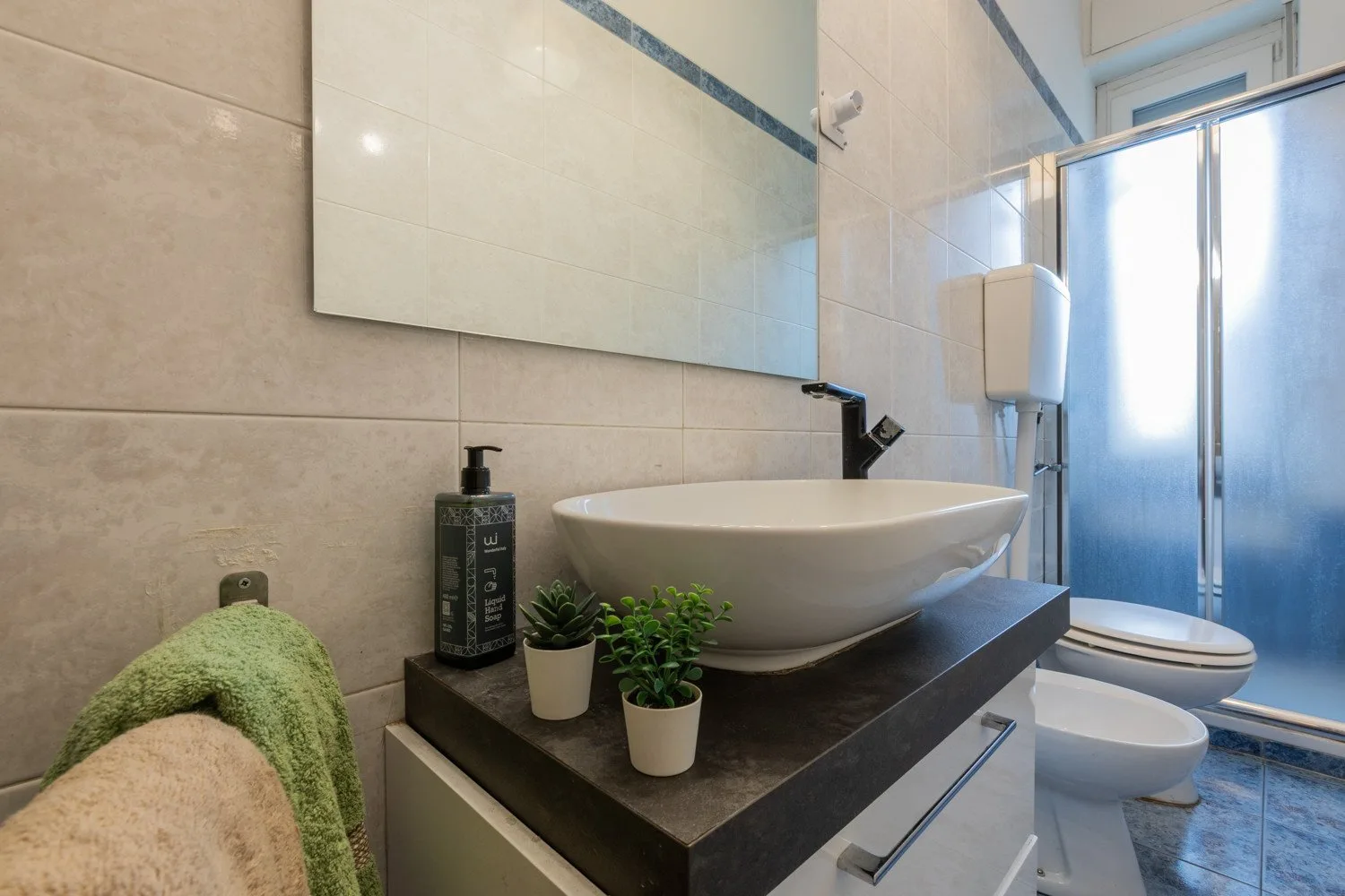 Un baño con azulejos cuenta con un amplio lavabo, inodoro y ducha de cristal.