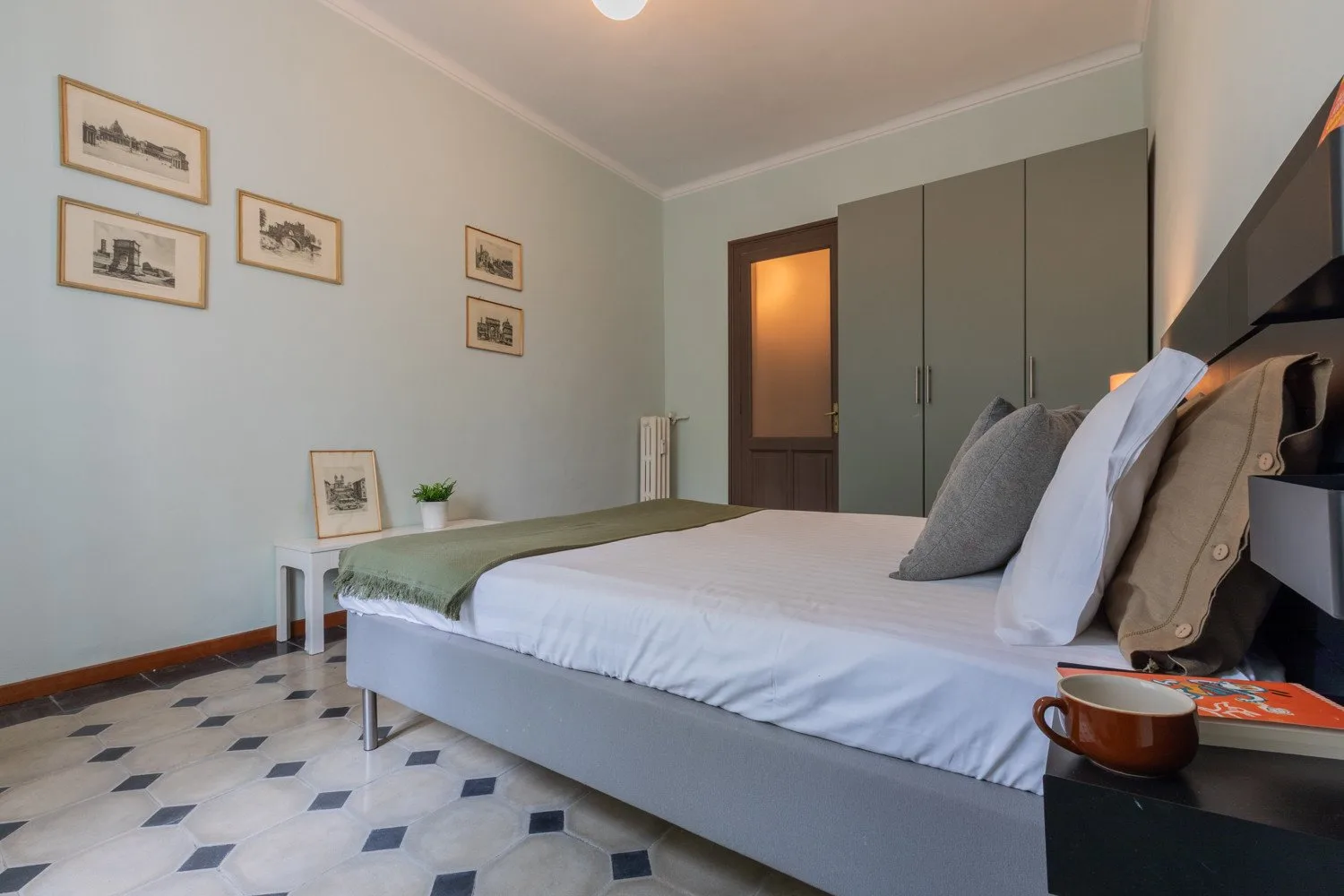 Un dormitorio con una cama tendida y cuadros enmarcados en la pared.