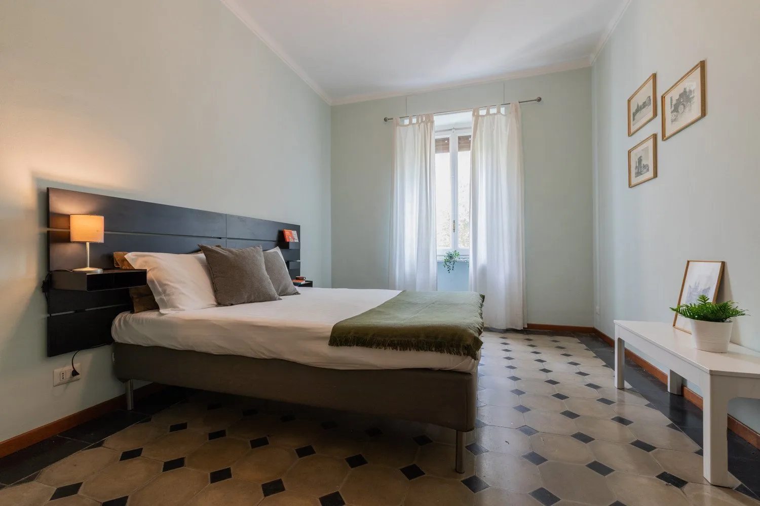 Un dormitorio con una cama, una ventana con cortinas y una planta pequeña.