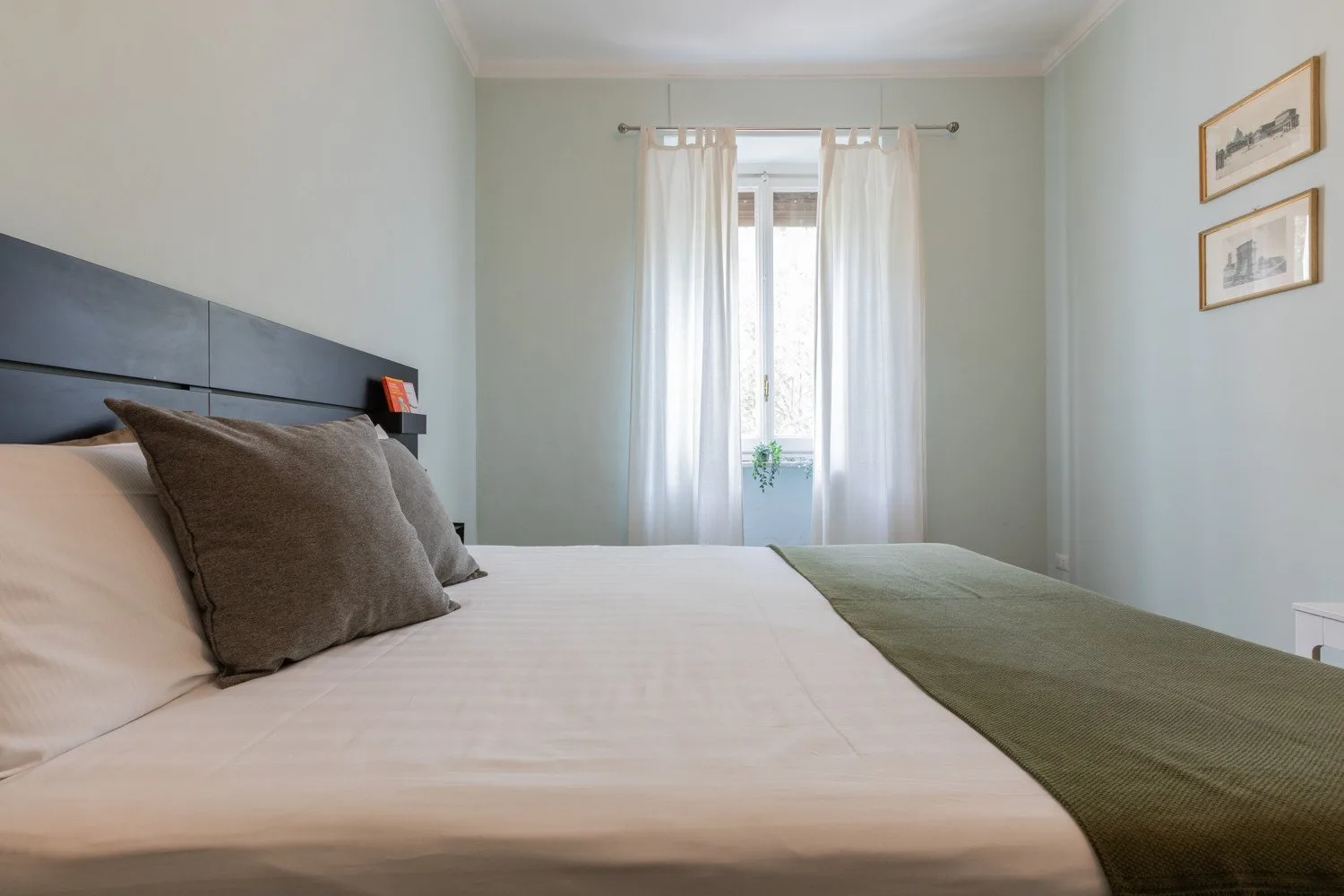 Un dormitorio con una cama bien tendida y una ventana con cortinas translúcidas.
