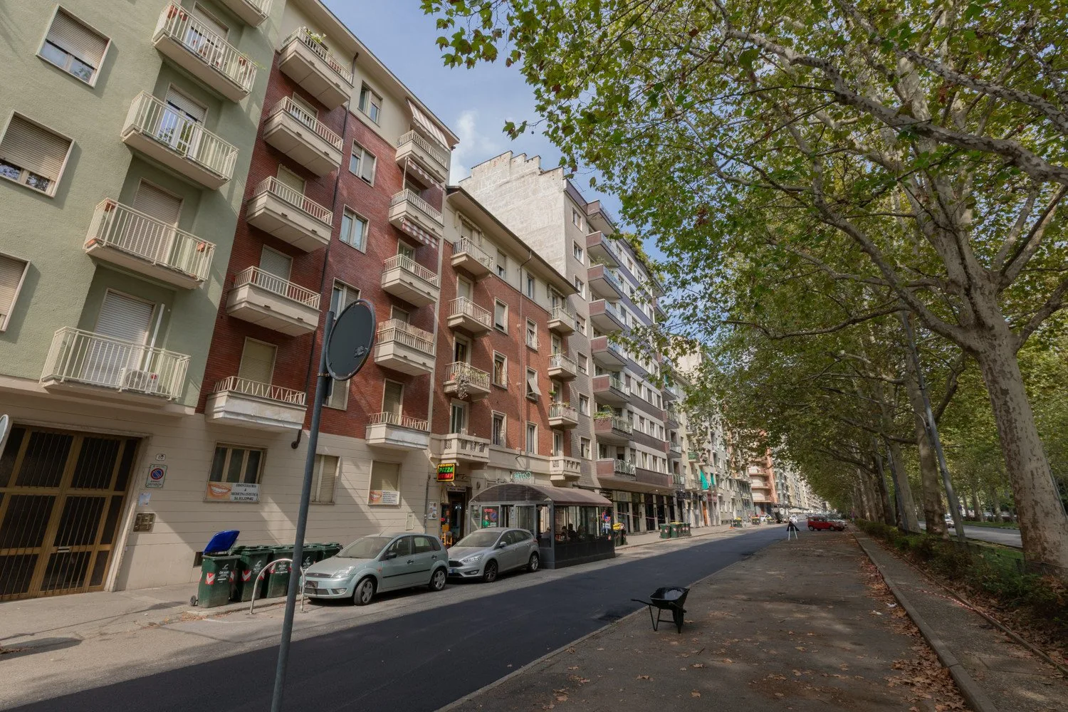 Una calle arbolada de la ciudad con edificios de apartamentos y coches aparcados.