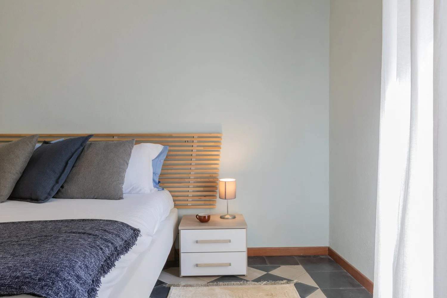 Un dormitorio con una cama, una mesita de noche y una ventana luminosa.