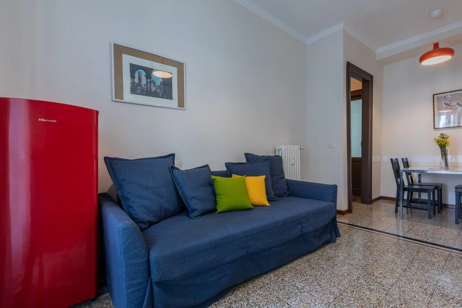 Una sala de estar con asientos azules junto a un refrigerador rojo y un comedor.