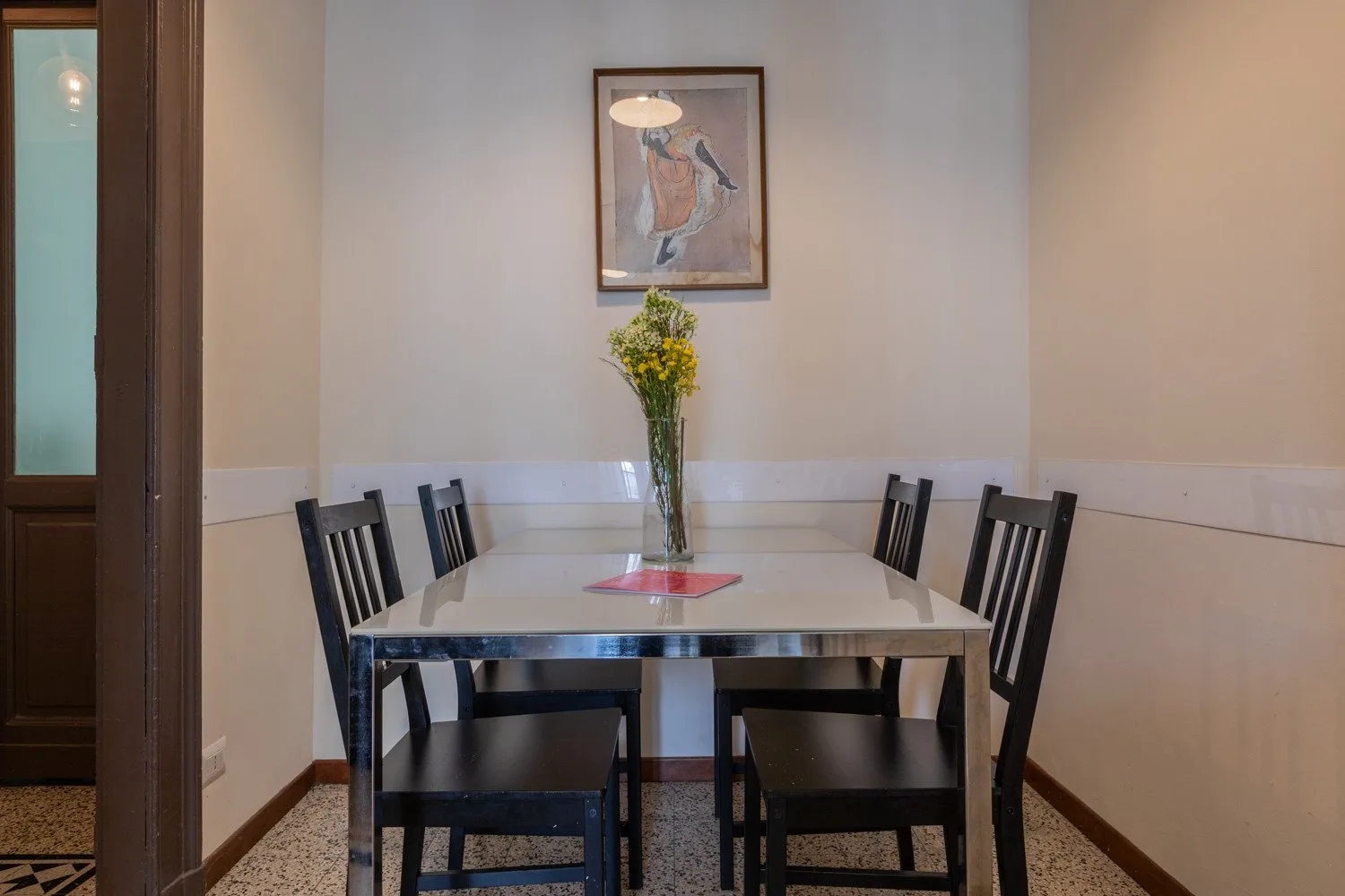 Un comedor tiene una mesa rectangular con asientos oscuros y un jarrón con flores.