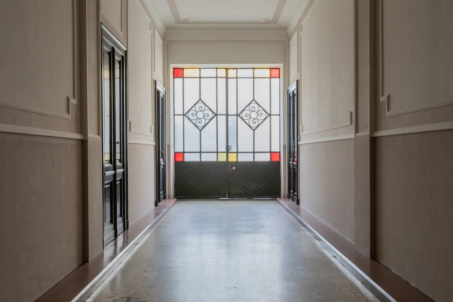 Un pasillo estrecho conduce a una puerta de vidrio decorada con motivos geométricos.
