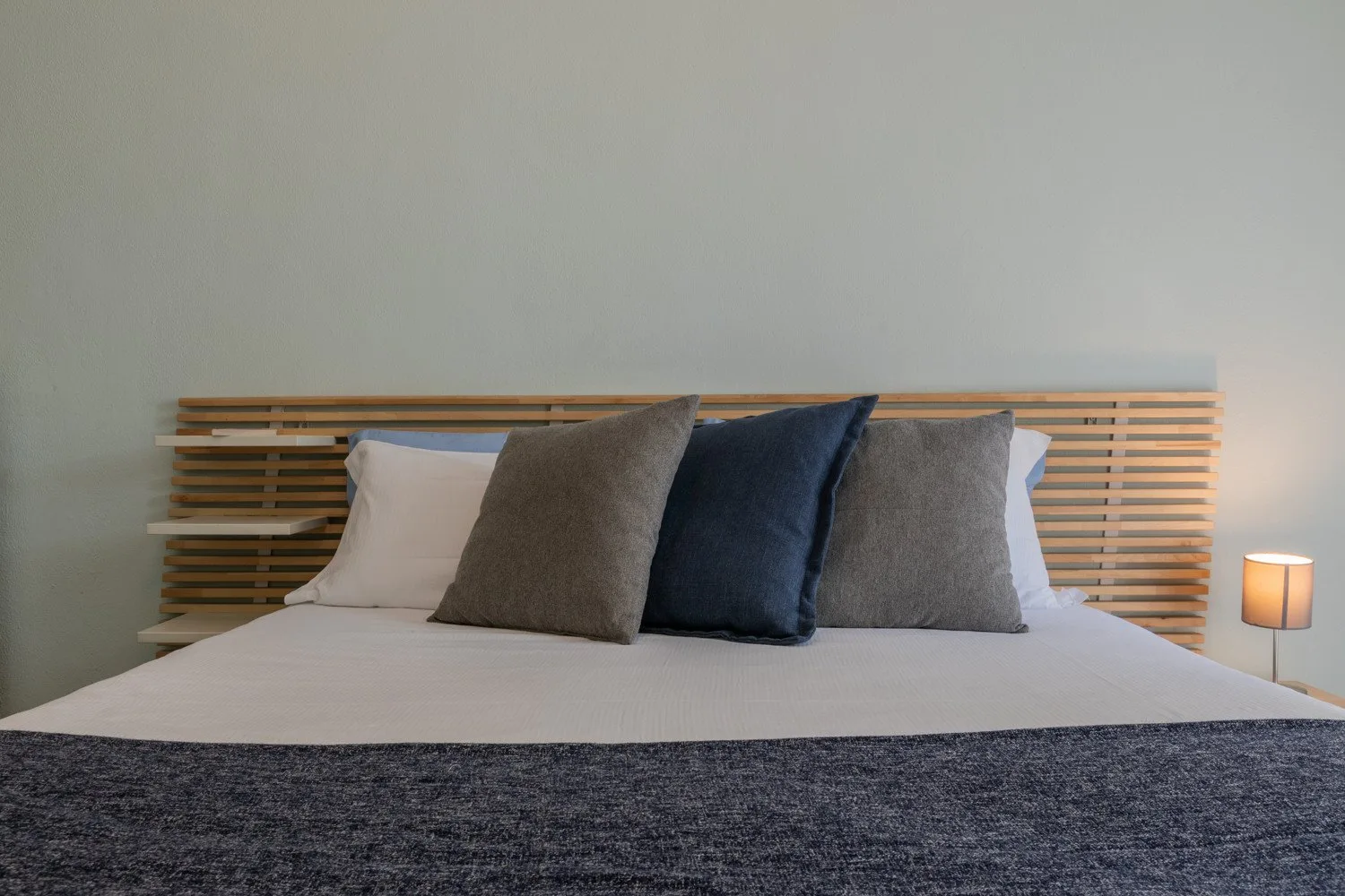 Una cama bien hecha con varias almohadas y una manta oscura.