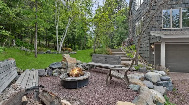 An outdoor patio with a fire pit, seating, and a wooded yard.