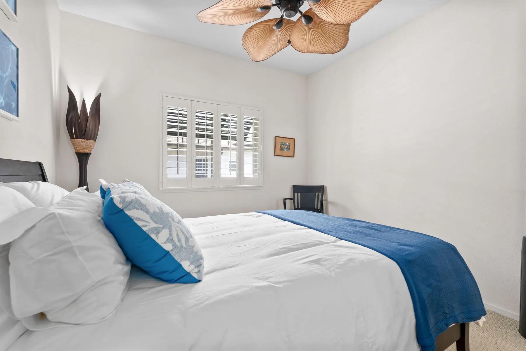 A bedroom with a bed dressed in white linens and blue accents.