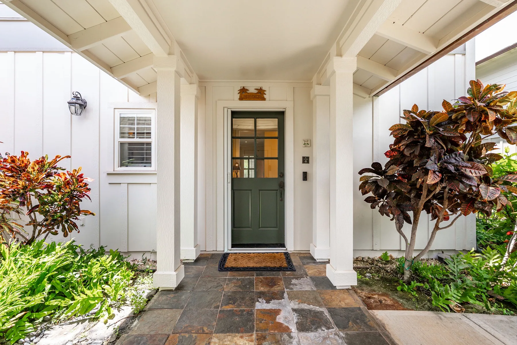 A covered front entry with a dark green door and stone walkway.