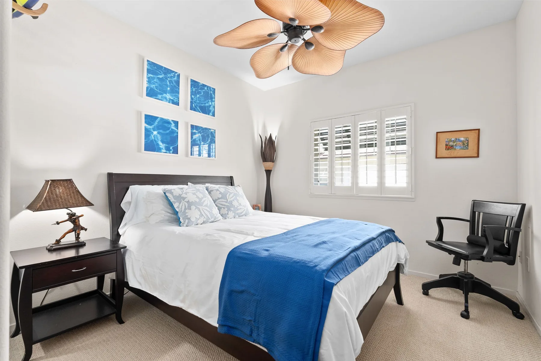 A bright bedroom with a bed dressed in white linens and a blue blanket.