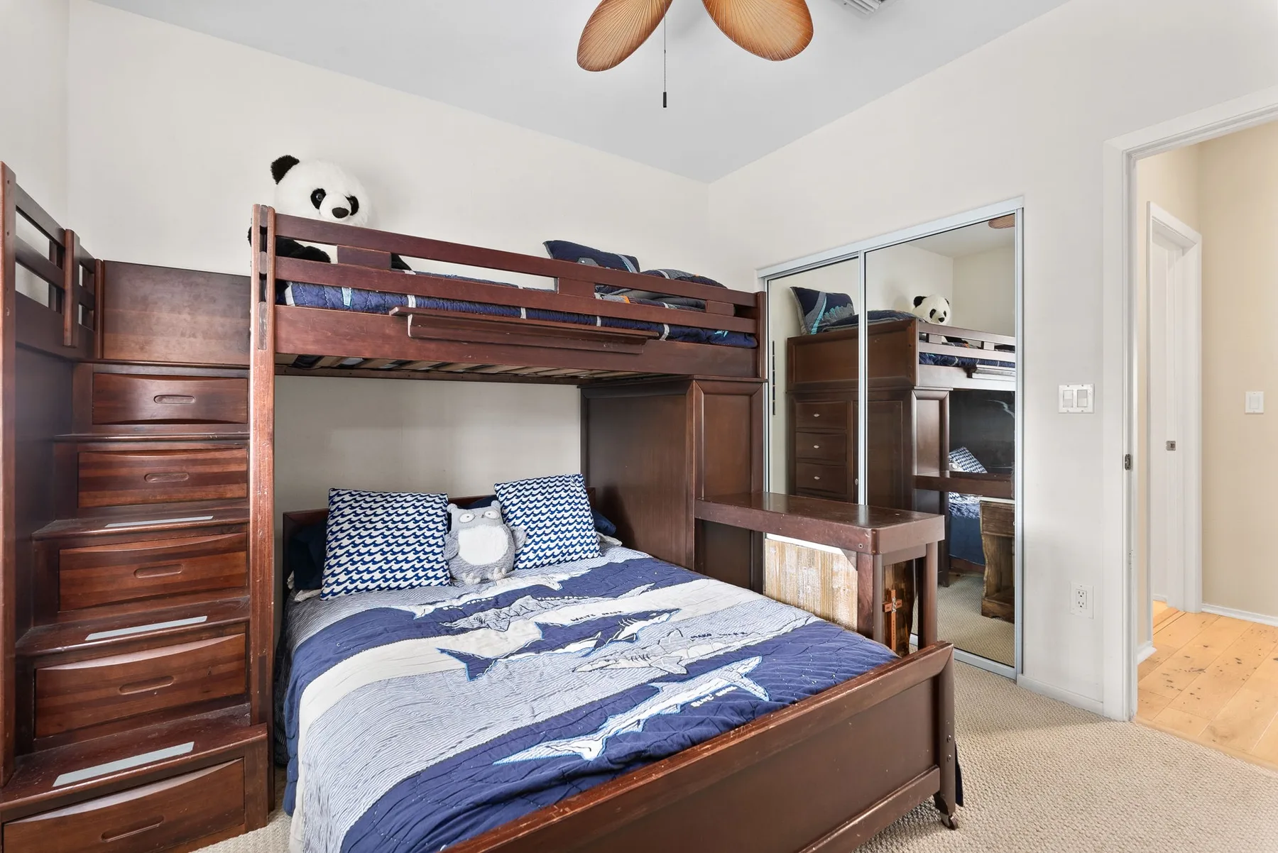 A bedroom with a wooden bunk bed, blue bedding, and mirrored closet doors.
