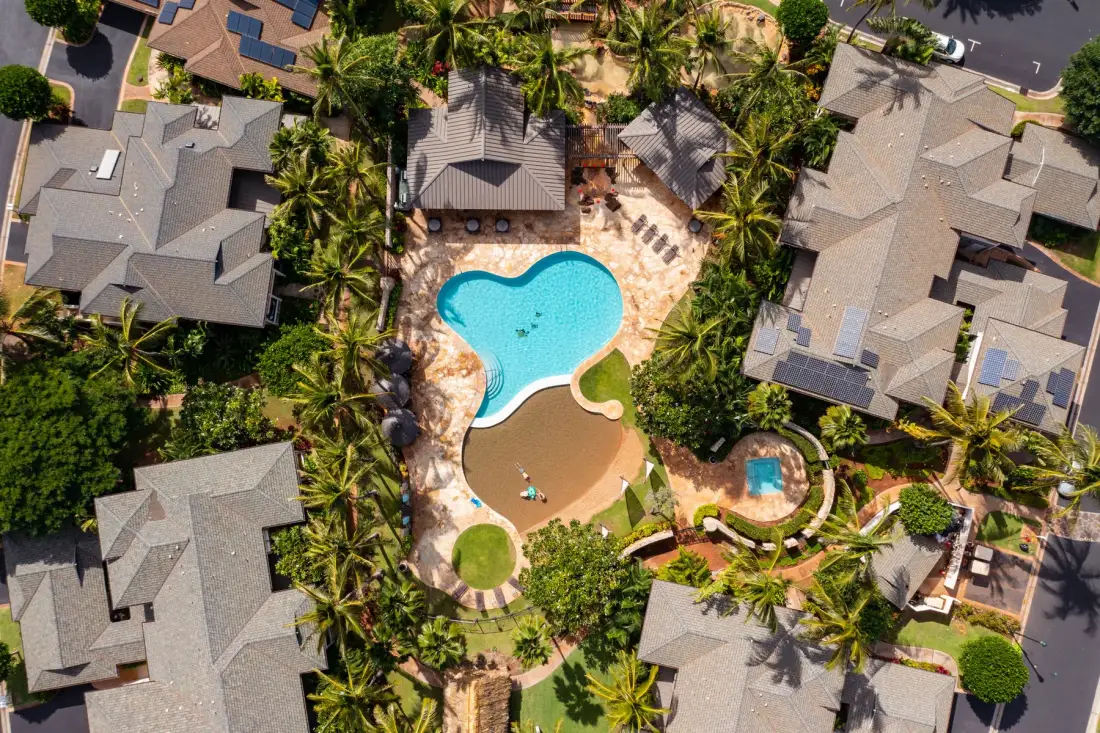 An aerial view of a resort pool surrounded by buildings and palm trees.